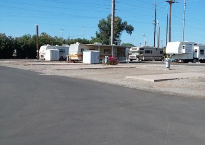 A photograph of the RV park grounds at Goldwater Estate RV park. The street is paved with white homes to the left of the street. Some homes have cars parks in the driveways.
